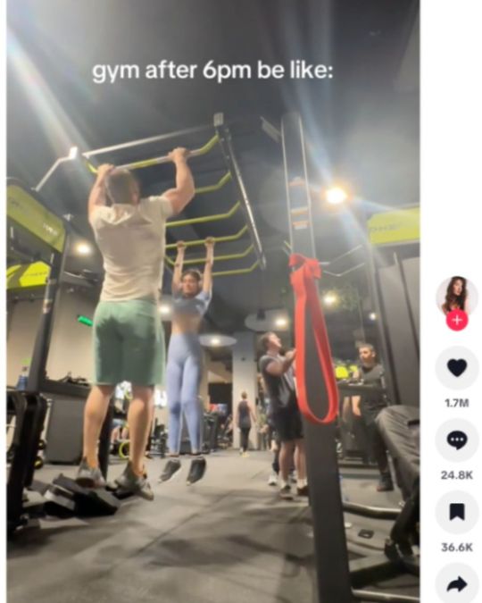 Still from a TikTok video of a man and a woman hanging from bars in a gym. The overlay text reads: “gym after 6pm be like:”