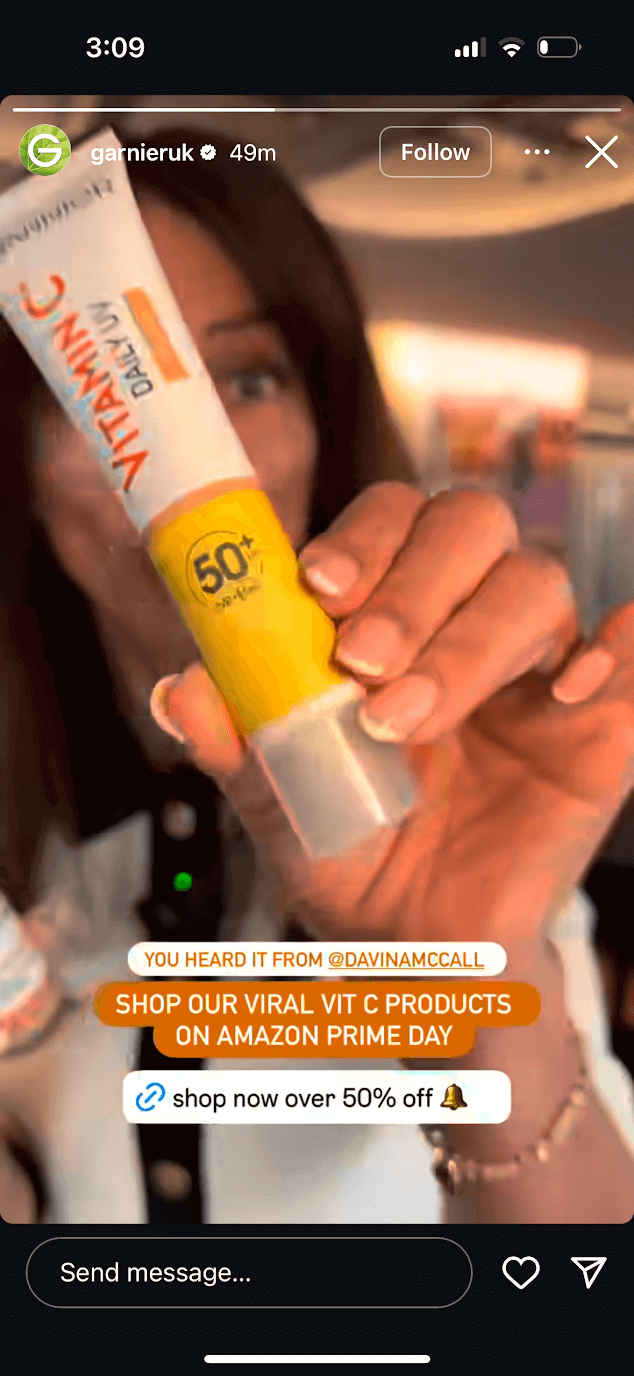Garnier UK Instagram Story featuring someone holding the brand's vitamin C sunscreen up to the camera and a link sticker text that reads "shop now over 50% off" and a bell emoji