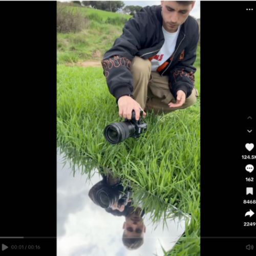 A still from a TikTok video of a man crouching down over a creek holding a Nikon camera over the water 