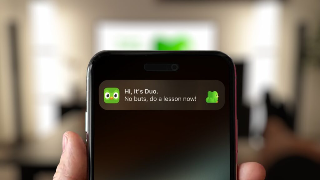 An image of a person holding their phone when a notification from the Duolingo app that says "no butts, do a lesson now!"