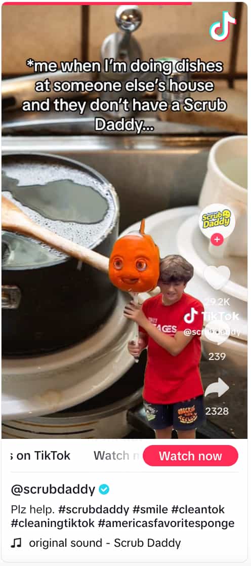 Scrub Daddy TikTok video showing someone holding up a fish-shaped sponge against a green screen background of a pile of dirty dishes