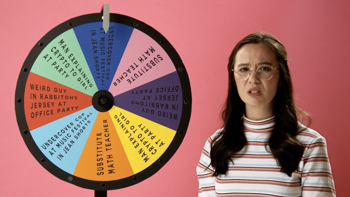 A still frame from Bailey Nelson’s brand film showing a person with glasses in front of a pink wall next to a wheel that spins with different options it lands on.