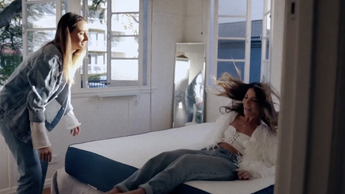 A still frame from Koala’s brand film showing a woman falling backward onto a Koala mattress while her friend looks on.