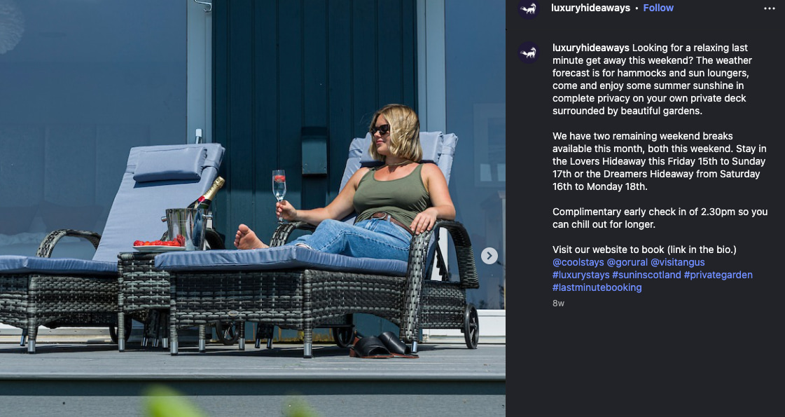 A woman relaxes on a wicker sun lounger with a glass of champagne outside a luxury retreat, with blue cushions and a private garden.