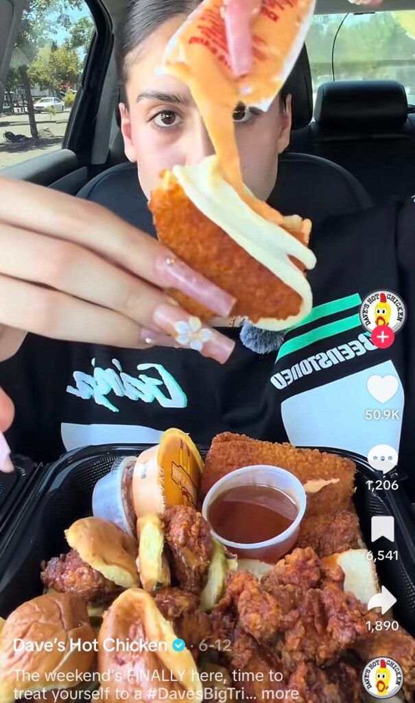 A woman holds a mozzarella stick while pouring sauce on it in a video from Dave’s Hot Chicken’s TikTok.