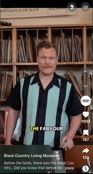 Man in striped shirt tells the pre-fame story of the Beatles among vinyl record shelves in a "Fab Four" history video.